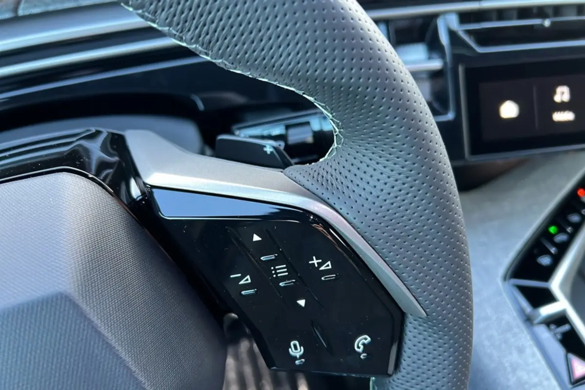 Gros plan sur le volant cuir perforé gris du Peugeot 3008 Hybrid 145 GT avec commandes multifonctions et tableau de bord partiel.