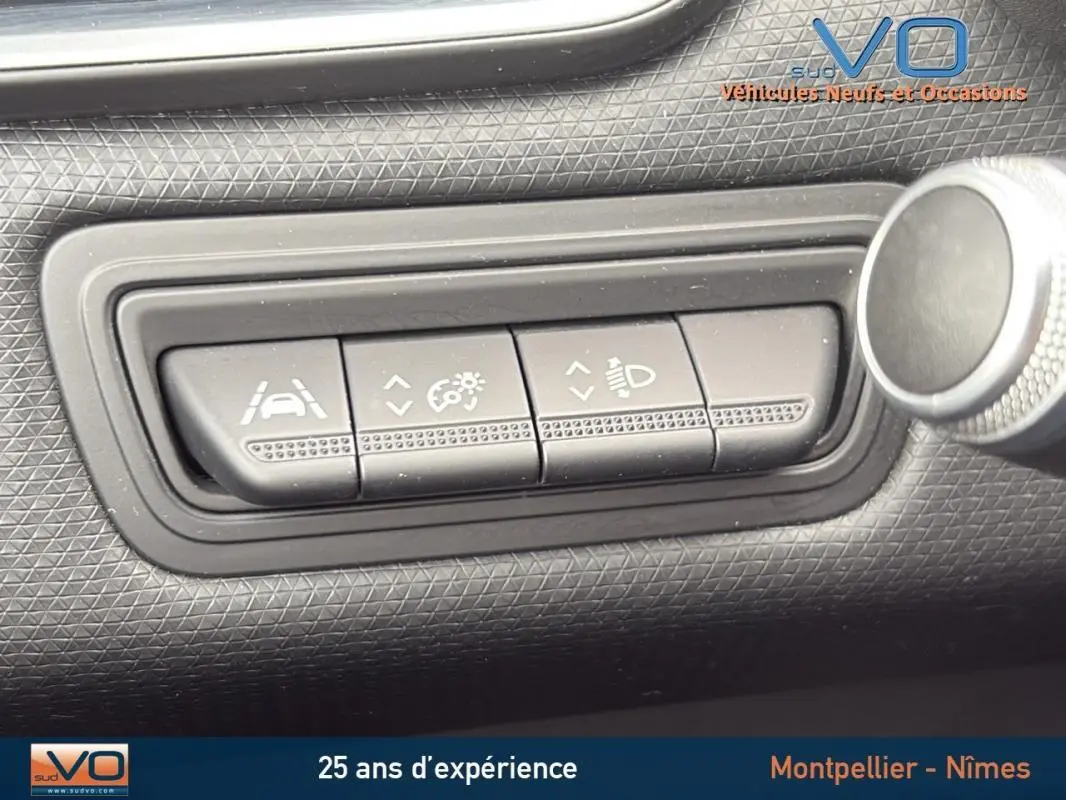 Gros plan sur les boutons de réglage d'aide à la conduite et des feux du tableau de bord d'une Renault Clio gris foncé.