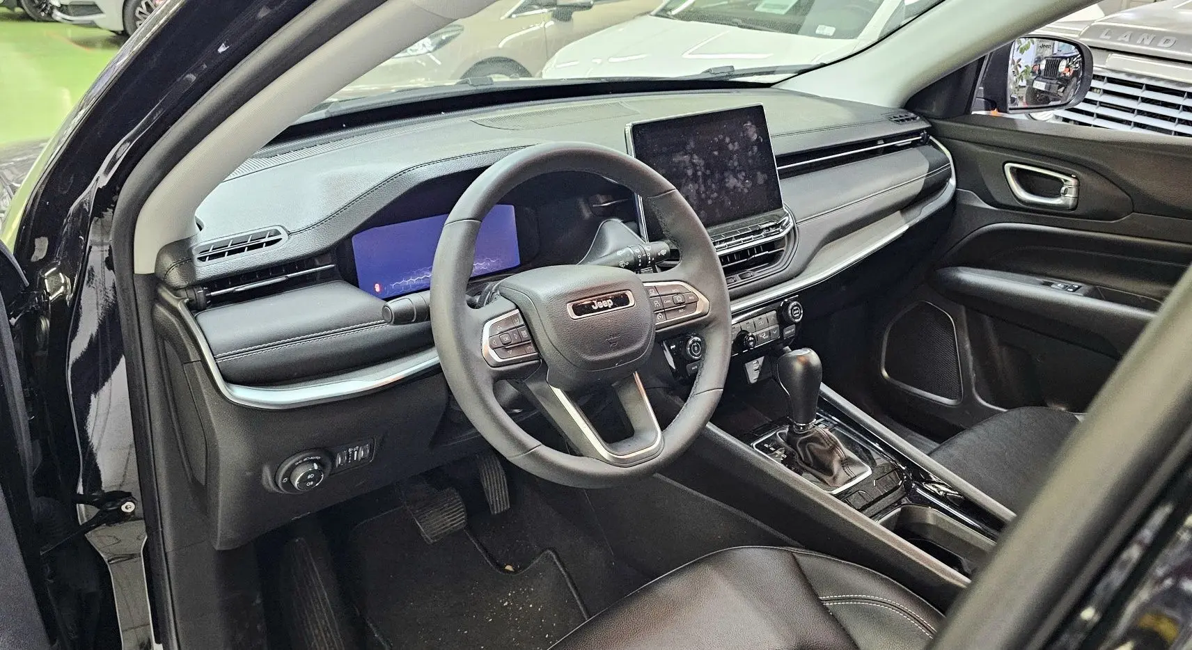Intérieur noir du Jeep Compass 2023 vu côté conducteur, avec tableau de bord moderne et écran tactile central.