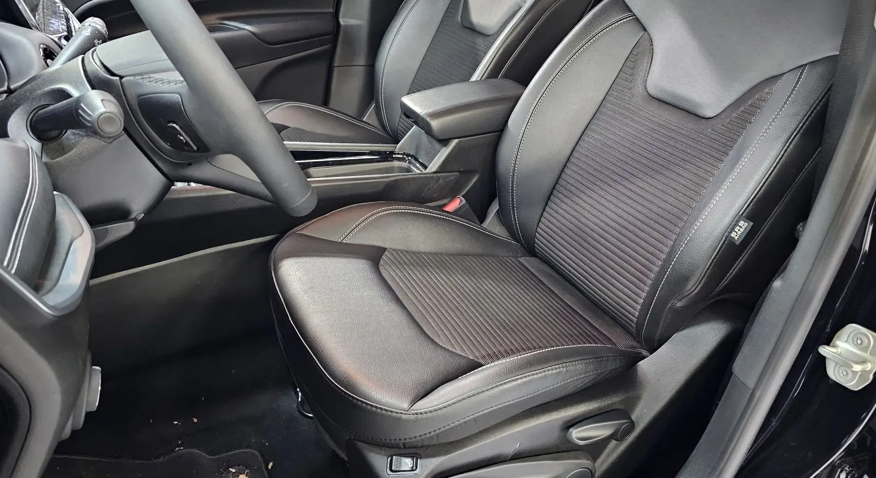 Vue rapprochée du siège conducteur noir en cuir et tissu du Jeep Compass 2023 avec accoudoir central et volant partiel.