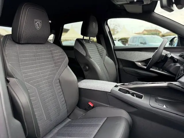 Vue intérieure côté gauche du Peugeot 3008 Hybrid 145 GT 2025, sellerie tissu Uziris gris avec logo Peugeot brodé sur appuie-tête.