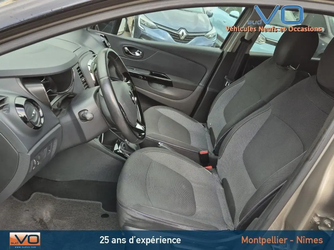 Intérieur avant du Renault Captur gris 2014, sièges tissu gris, volant cuir, tableau de bord et console visibles.