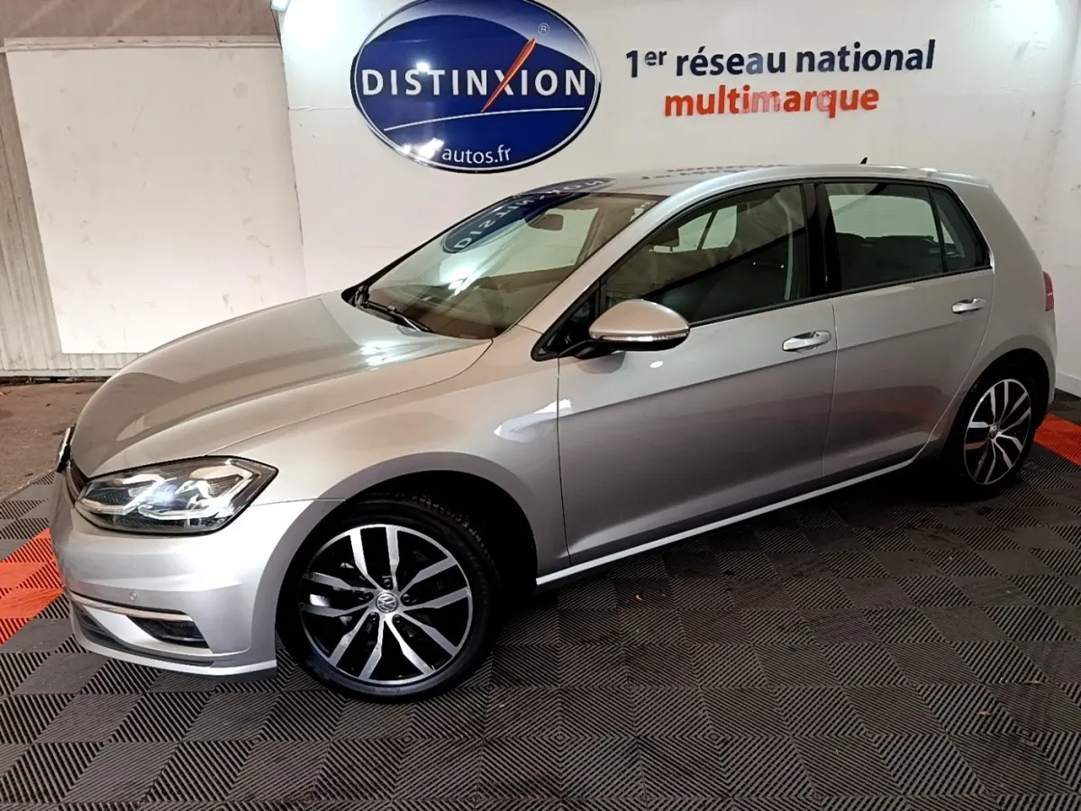 Volkswagen Golf gris clair vue de profil côté gauche, avec jantes alliage et phares allumés.