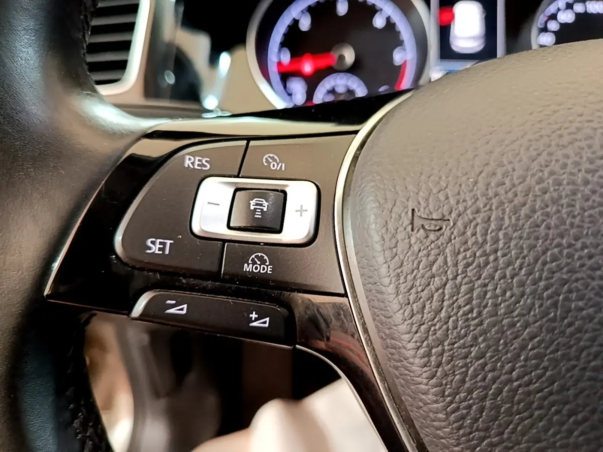 Gros plan sur les commandes du volant cuir gris de la Volkswagen Golf 1.6 TDI 2017 avec tableau de bord lumineux en arrière-plan.