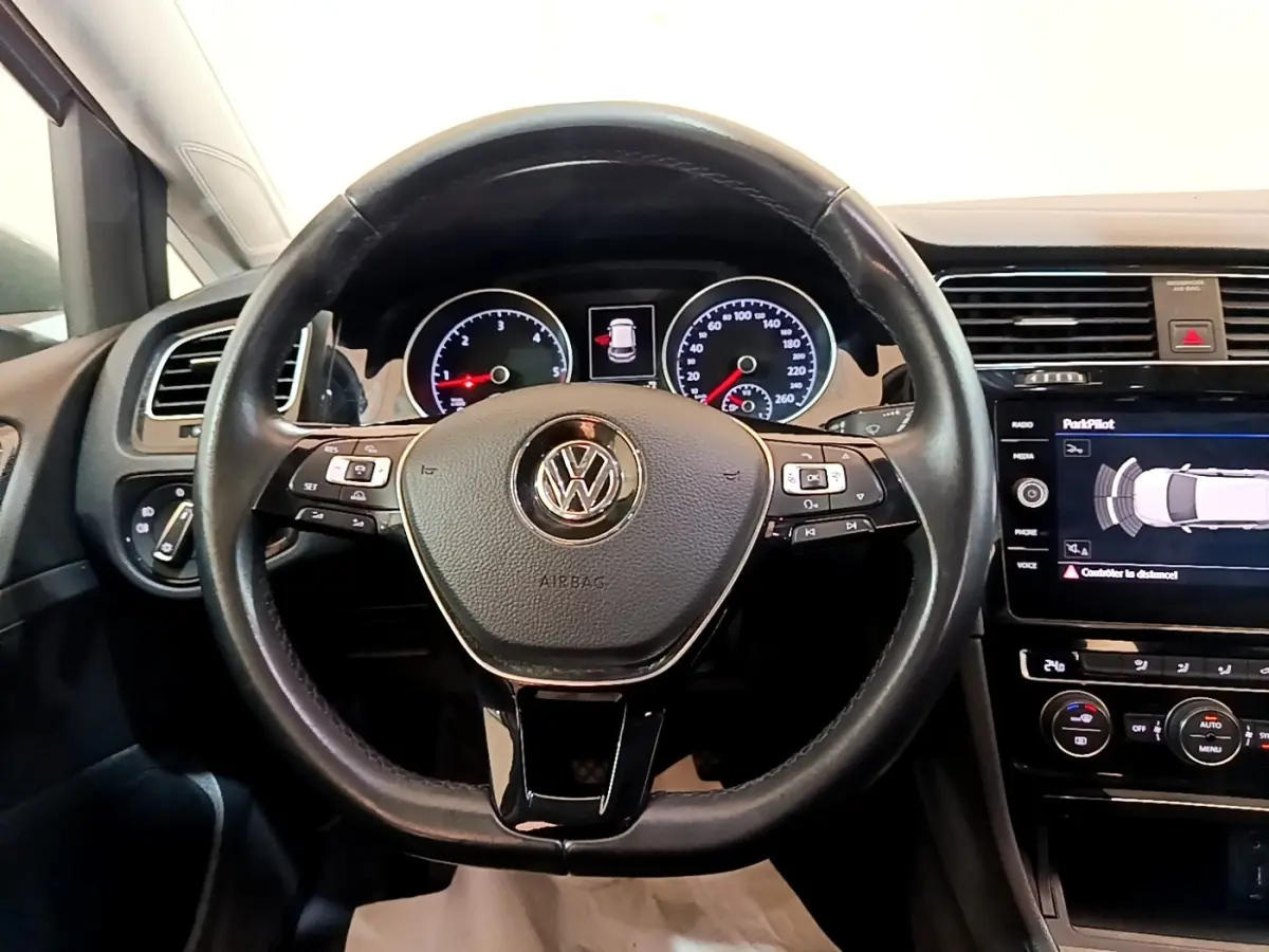 Vue frontale du volant cuir noir de la Volkswagen Golf 2017 avec tableau de bord et écran tactile affichant l'aide au stationnement.