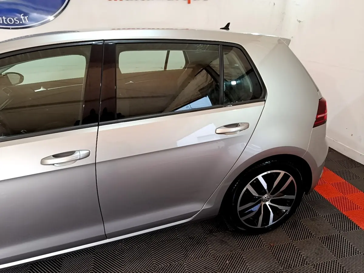 Vue latérale côté gauche d'une Volkswagen Golf gris clair avec jantes alliage et poignées de porte chromées.