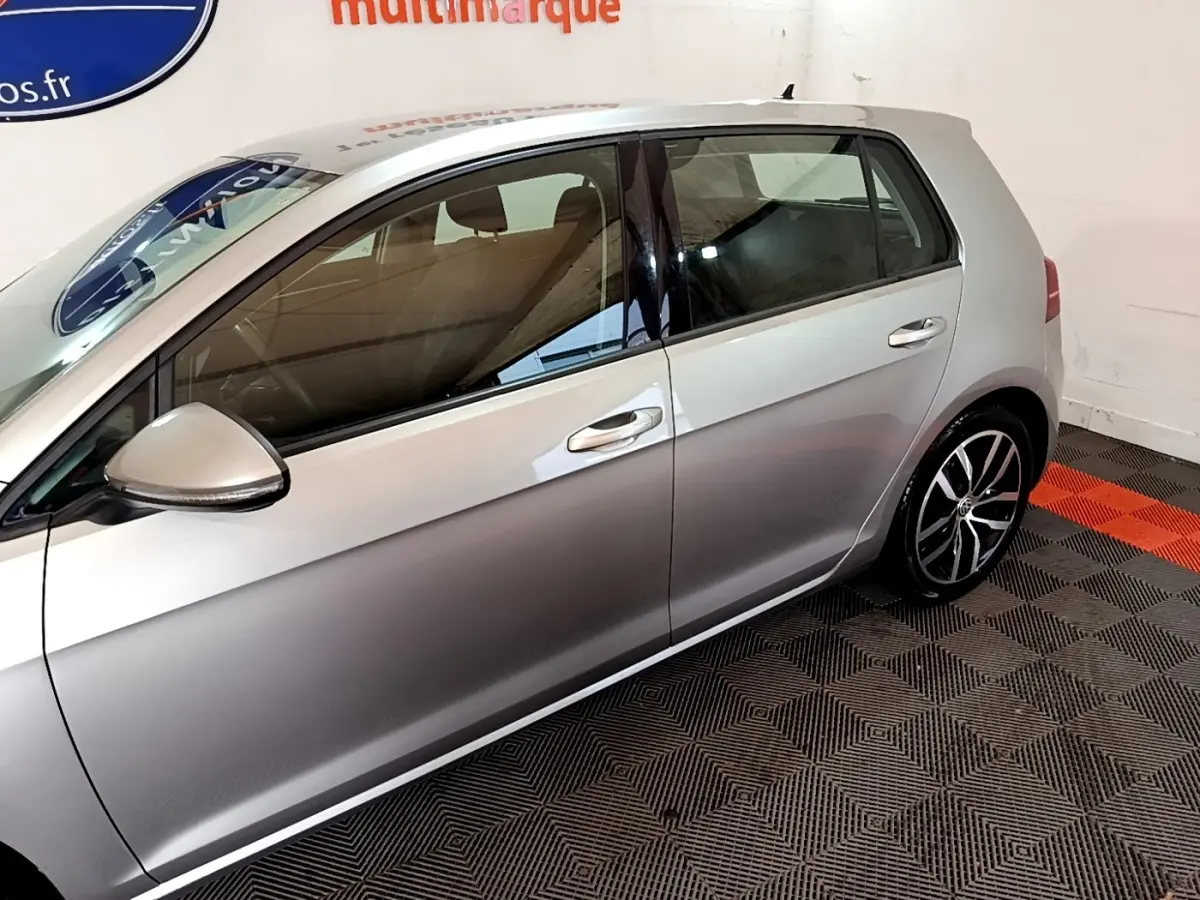 Profil côté gauche d'une Volkswagen Golf gris clair 2017, avec jantes alliage et rétroviseur électrique intégré.