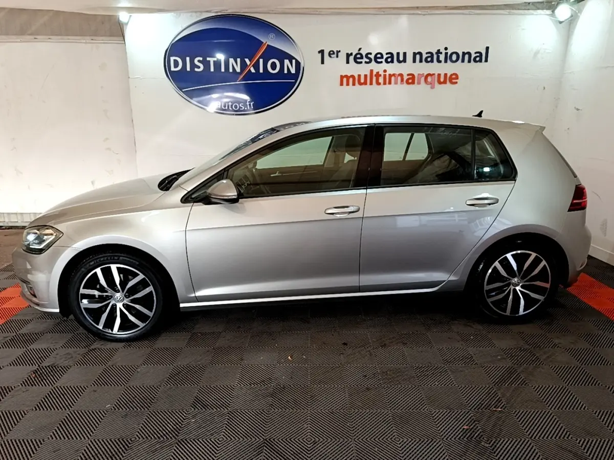 Profil côté gauche d'une Volkswagen Golf gris clair 2017, avec jantes alliage et poignées de porte chromées.