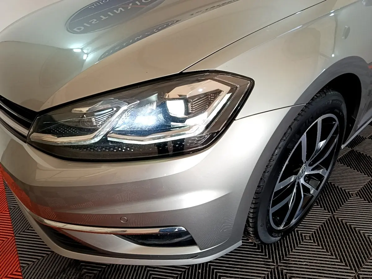 Gros plan sur l'avant droit d'une Volkswagen Golf gris clair, mettant en valeur le phare LED et la jante noire.