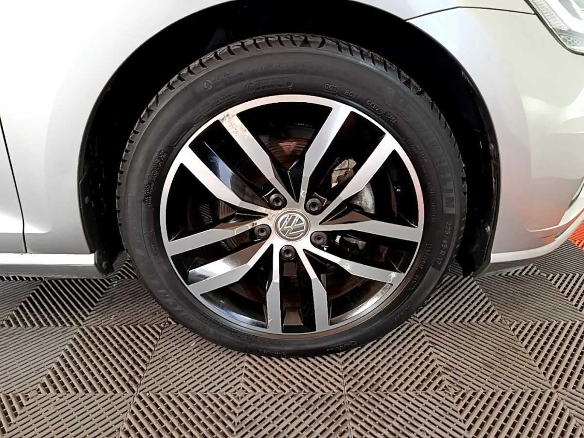 Gros plan sur la roue avant droite d'une Volkswagen Golf gris clair avec jante alliage bicolore.