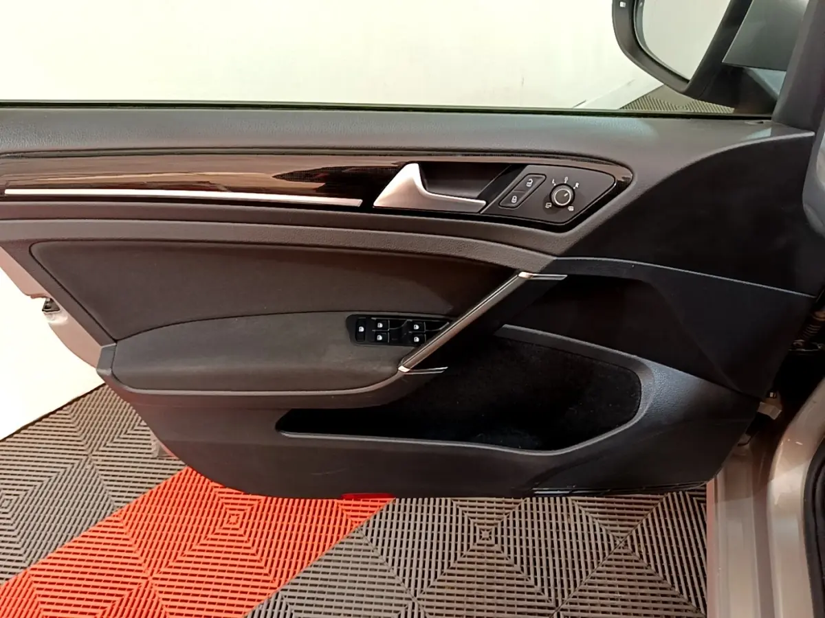 Vue du panneau de porte côté gauche de la Volkswagen Golf gris clair, avec commandes électriques et insert décoratif brillant.