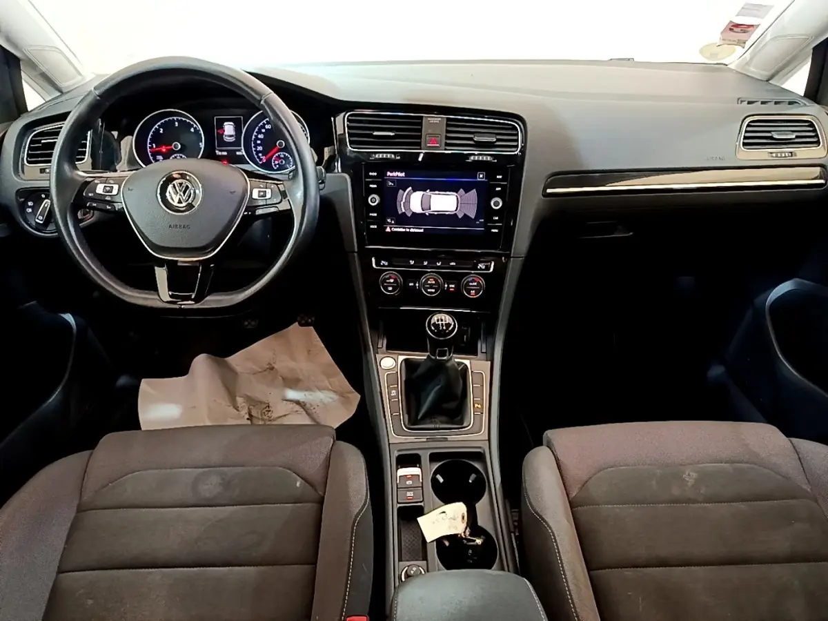 Vue intérieure avant de la Volkswagen Golf 1.6 TDI 2017, tableau de bord noir avec écran tactile et volant cuir multifonctions.
