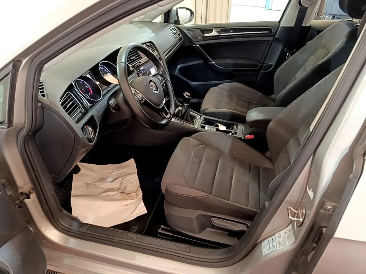 Vue intérieure côté conducteur de la Volkswagen Golf gris clair 2017, montrant sièges et tableau de bord noir.