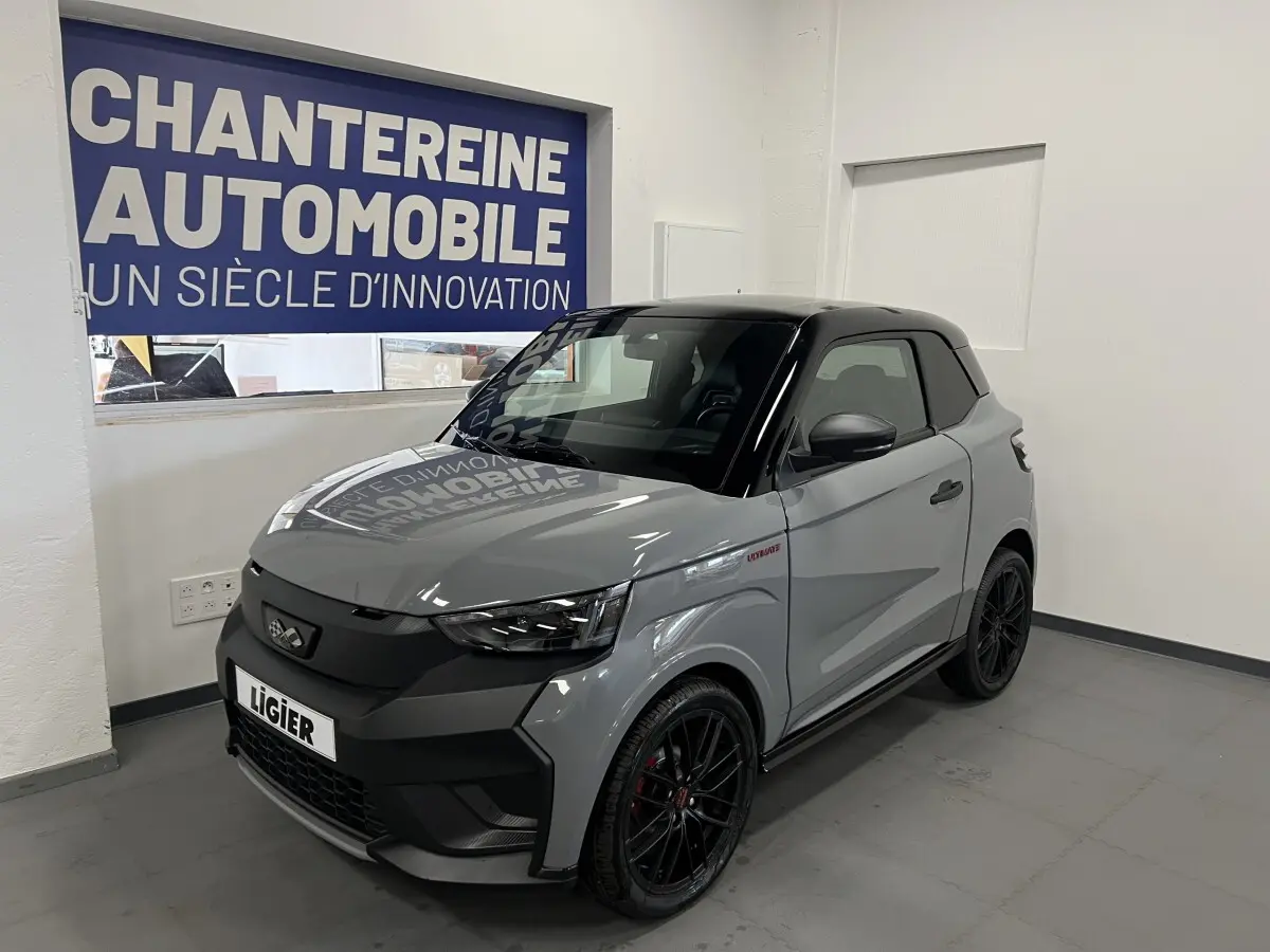 Vue 3/4 avant droite d'une Ligier JS50 0.5 REVO D+ Ultimate gris avec toit noir et jantes noires en showroom.