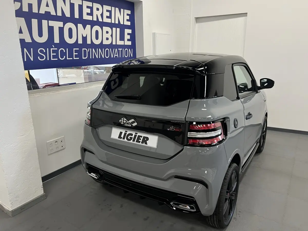 Vue 3/4 arrière droite d'une Ligier JS50 grise avec toit noir brillant et feux arrière LED en intérieur showroom.