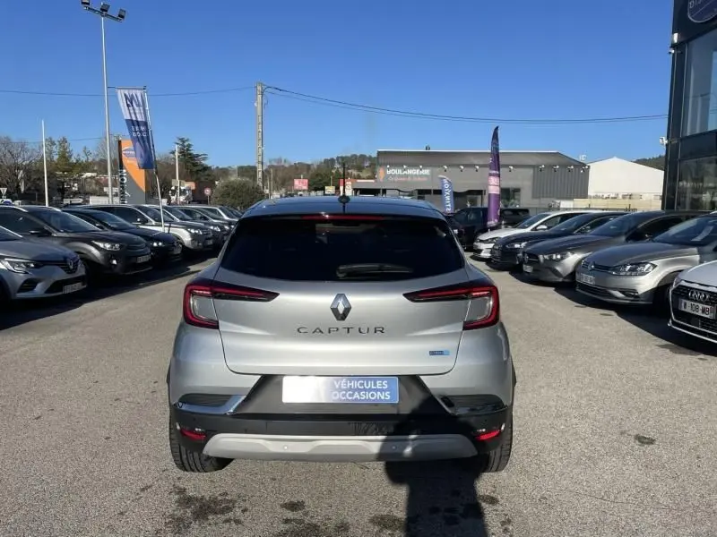 Vue arrière d'un Renault Captur gris métal 2022, version hybride, garé en extérieur sur un parking de voitures d'occasion.