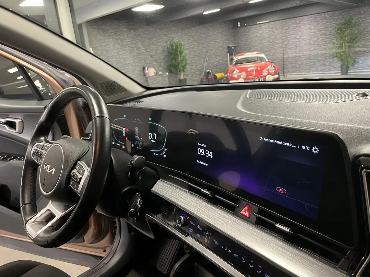 Intérieur du Kia Sportage marron 2022, vue côté conducteur sur le tableau de bord numérique et volant cuir.