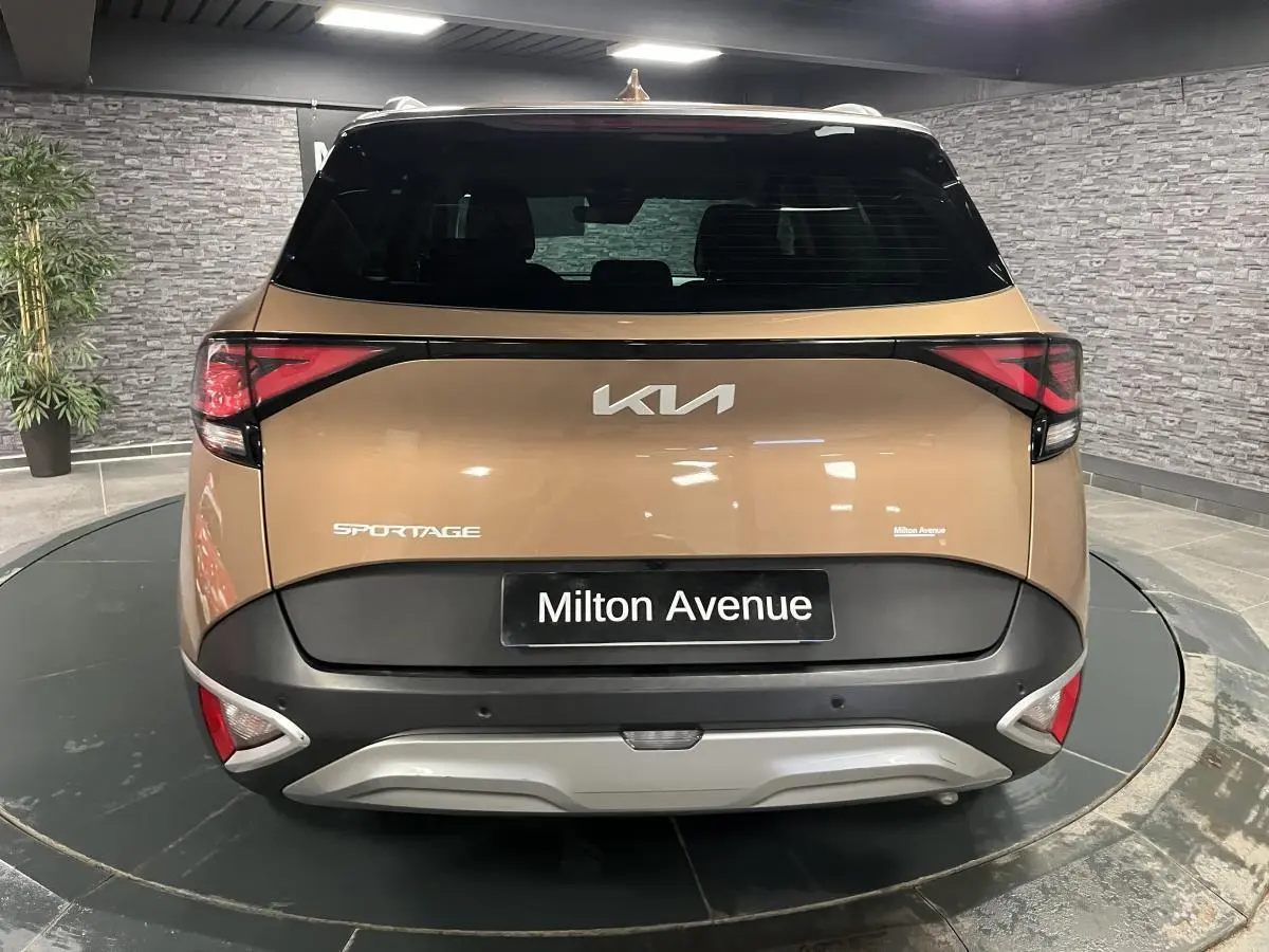 Vue arrière d'un KIA Sportage marron métallisé avec bouclier noir et plaque Milton Avenue visible en intérieur showroom.