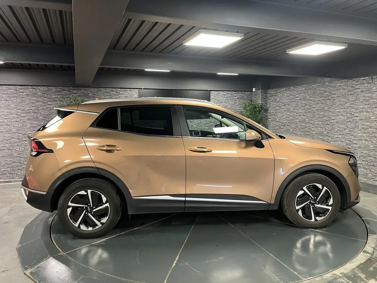 Profil droit d'un KIA SPORTAGE marron métallisé 2022 avec jantes alliage 17 pouces et protections noires laquées.