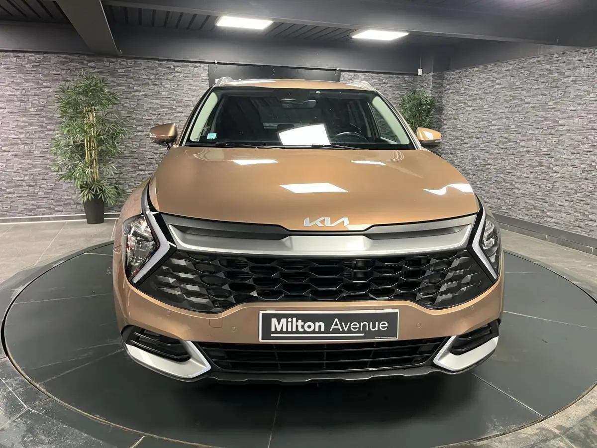 Vue frontale d'un Kia Sportage marron métallisé avec calandre noire et logo KIA sur le capot dans un showroom.