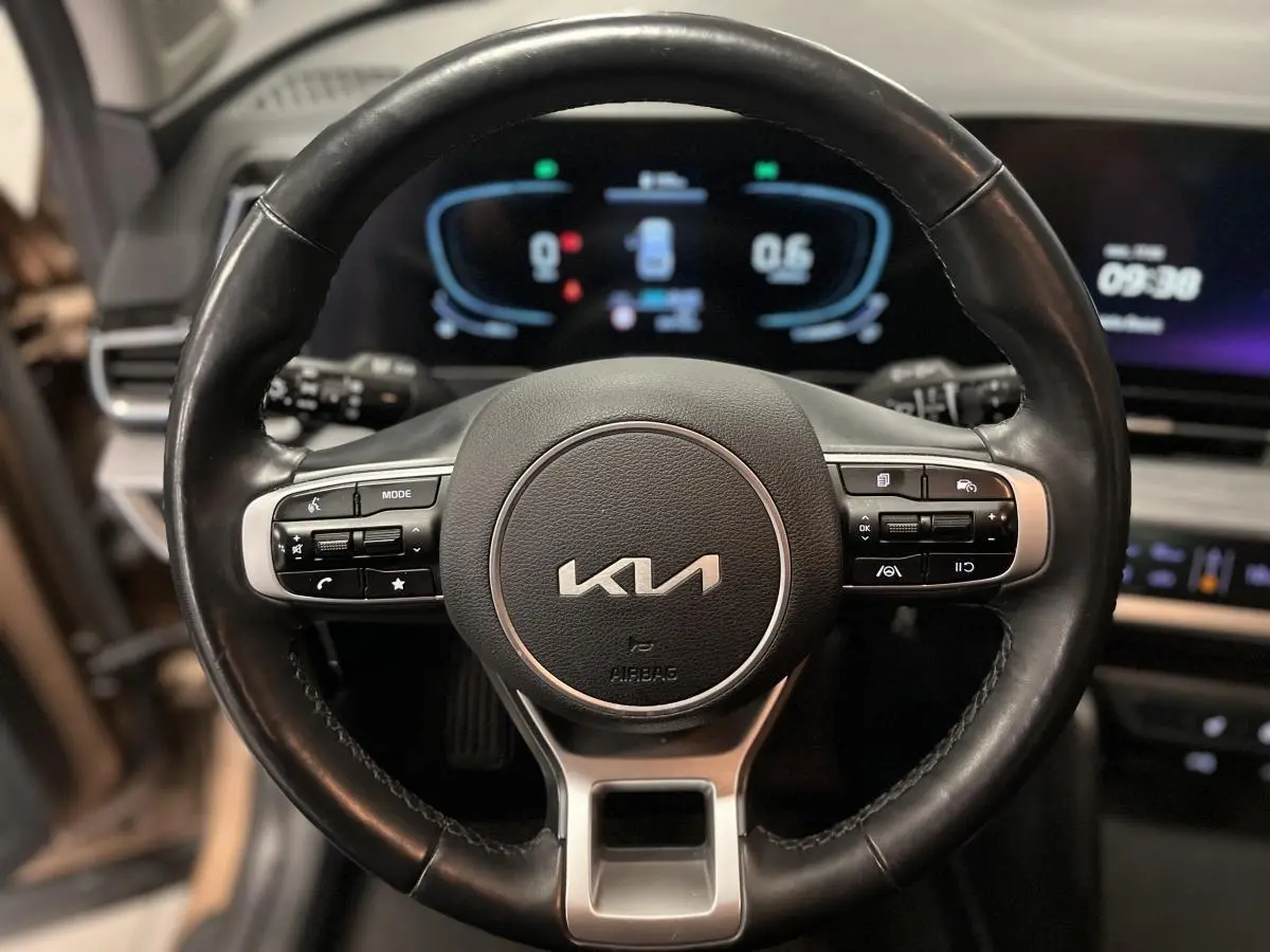 Volant cuir noir du Kia Sportage 2022 avec commandes intégrées et tableau de bord numérique lumineux en arrière-plan.