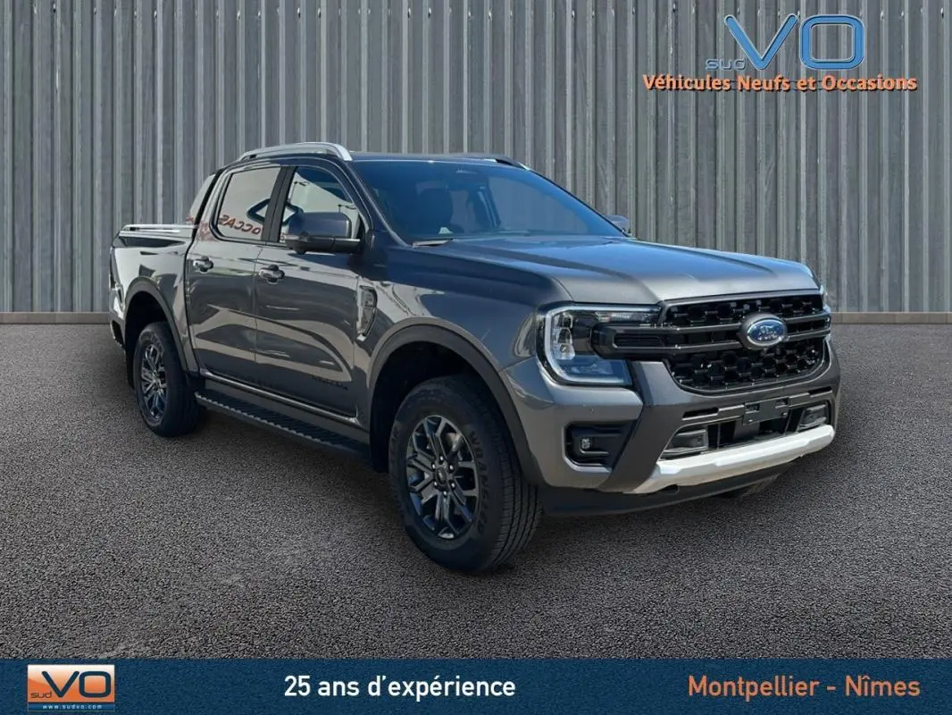 Ford Ranger gris en 3/4 avant droit, double cabine avec barres de toit et jantes alliage 17 pouces visibles.