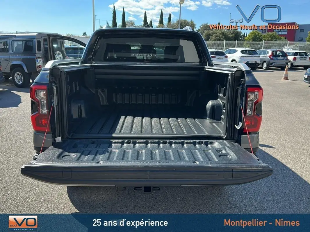Vue arrière du Ford Ranger gris 2025 avec benne ouverte et hayon déployé sur parking ensoleillé.