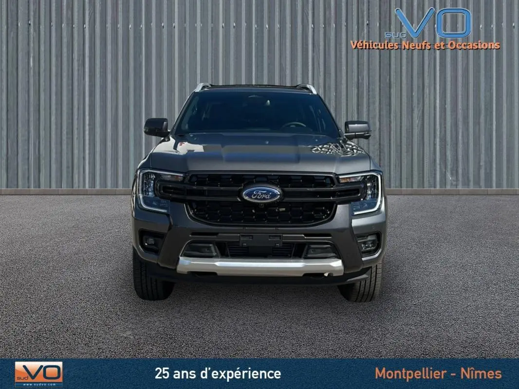 Vue frontale d'un Ford Ranger gris 2025 avec calandre noire, barres de toit et vitres surteintées visibles.