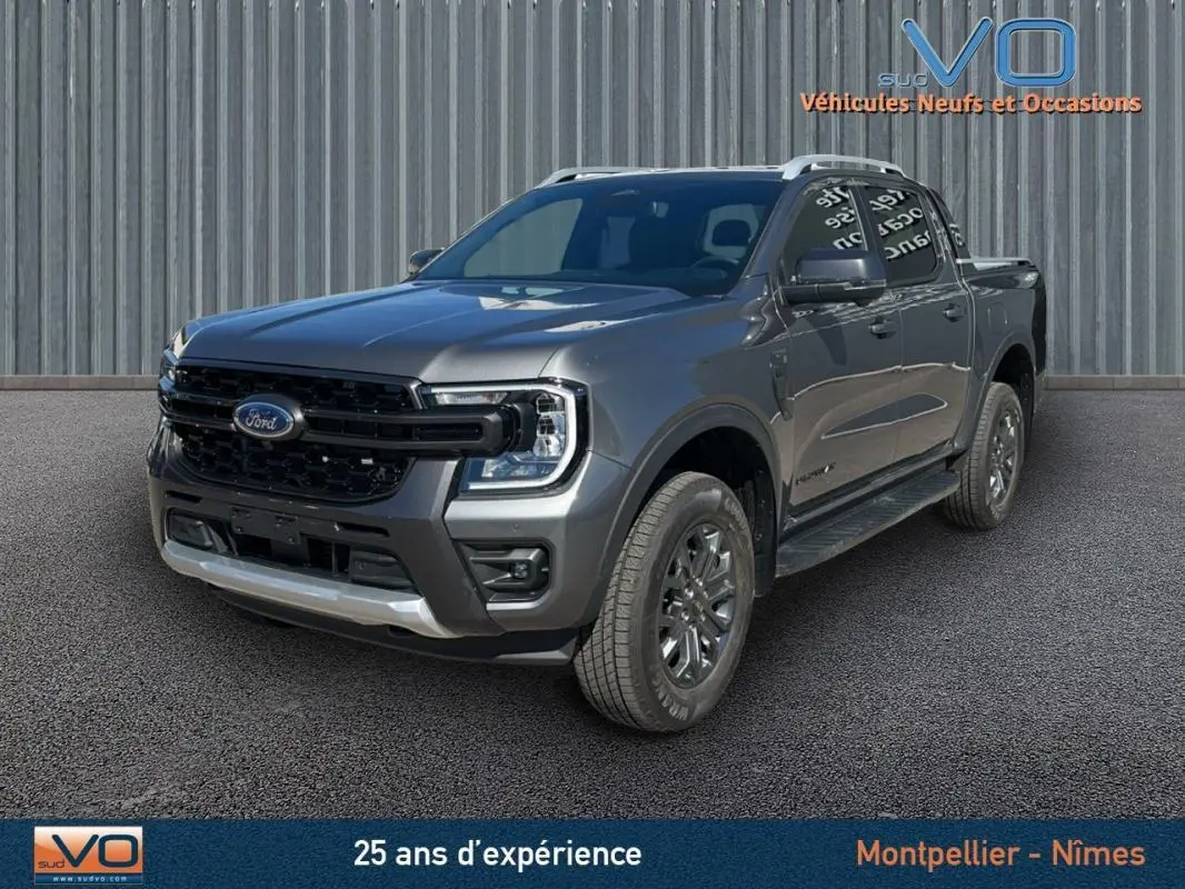 Ford Ranger Wildtrak gris en 3/4 avant droit, avec barres de toit et jantes alliage 17 pouces visibles.