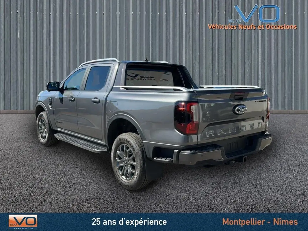 Ford Ranger Wildtrak gris en 3/4 arrière droit, avec barres de toit et vitres surteintées visibles.