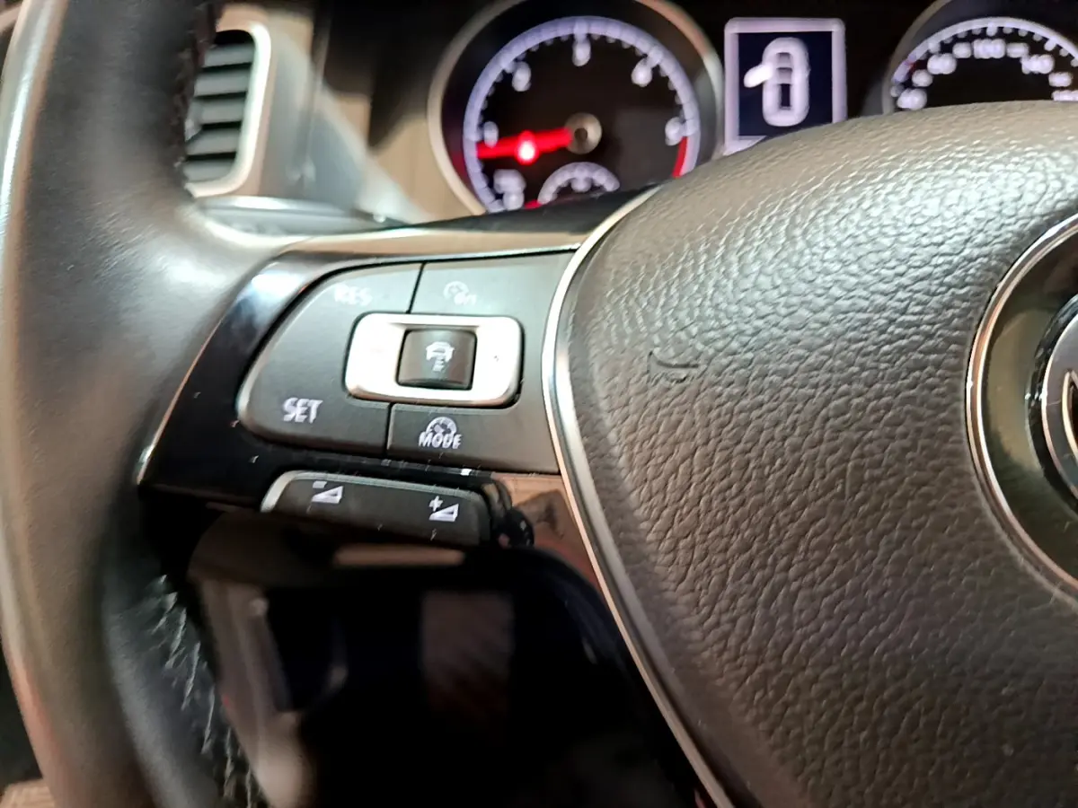 Gros plan sur le volant cuir noir de la Volkswagen Golf 2018, avec commandes multifonctions et tableau de bord éclairé.