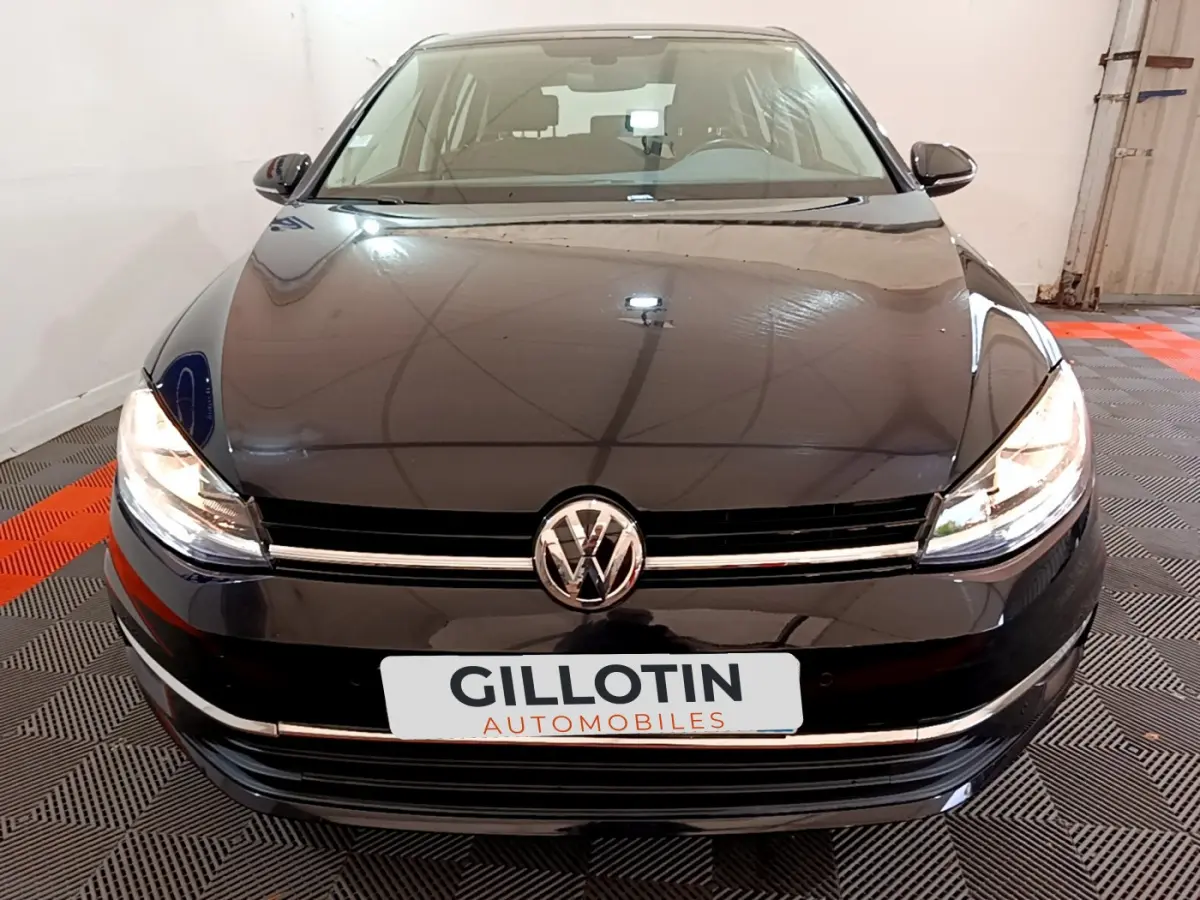 Vue frontale d'une Volkswagen Golf noire 2018 avec phares allumés et logo VW bien visible sur calandre.