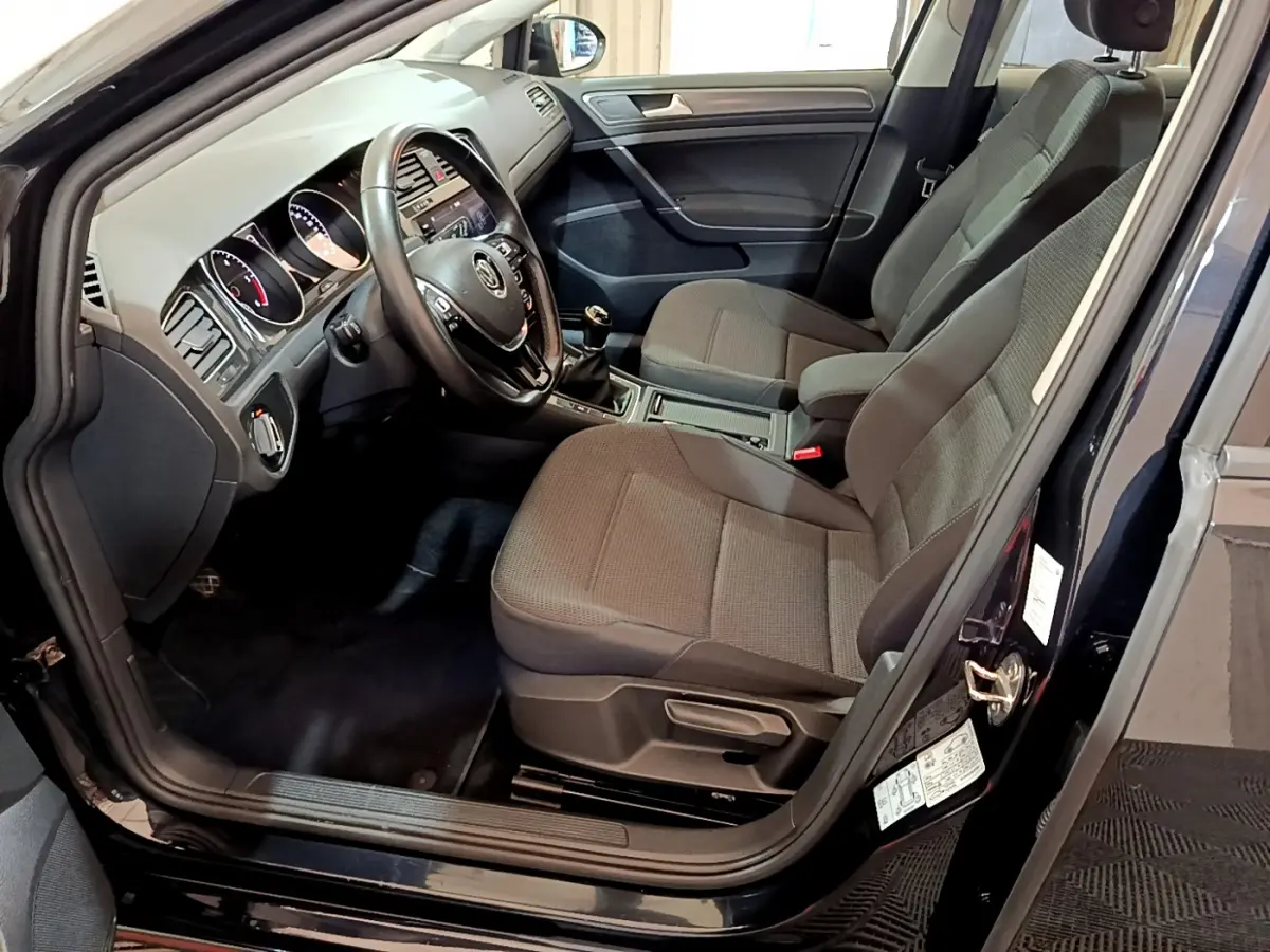 Intérieur avant droit d'une Volkswagen Golf noire 2018, sièges tissu gris et tableau de bord avec volant cuir.