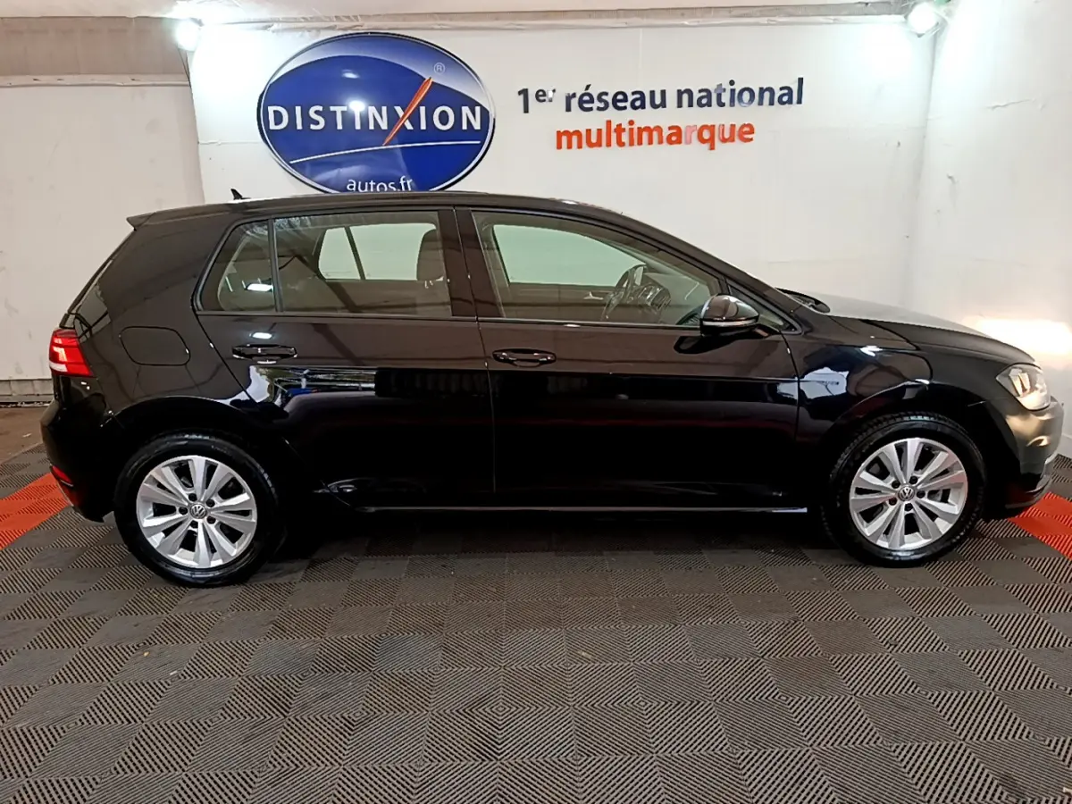 Profil côté gauche d'une Volkswagen Golf noire 2018, version Confort Business, dans un showroom lumineux.