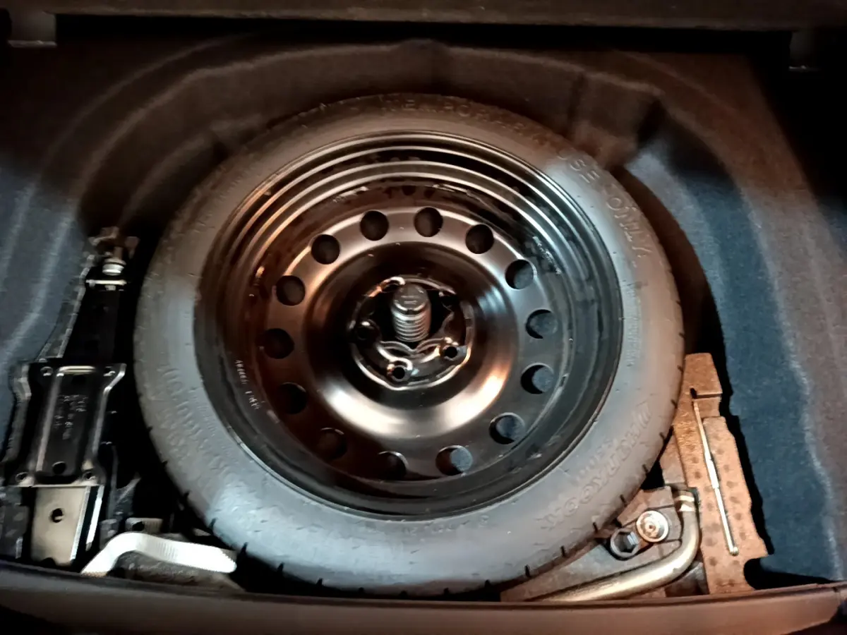 Roue de secours galette noire dans le coffre d'une Volkswagen Golf 2018, entourée des outils de changement.