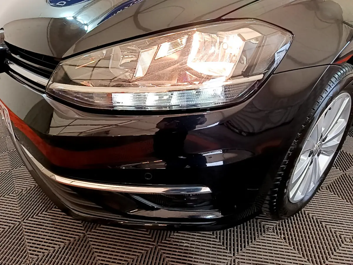 Gros plan sur l'avant droit d'une Volkswagen Golf noire 2018, mettant en valeur le phare allumé et la jante alu.