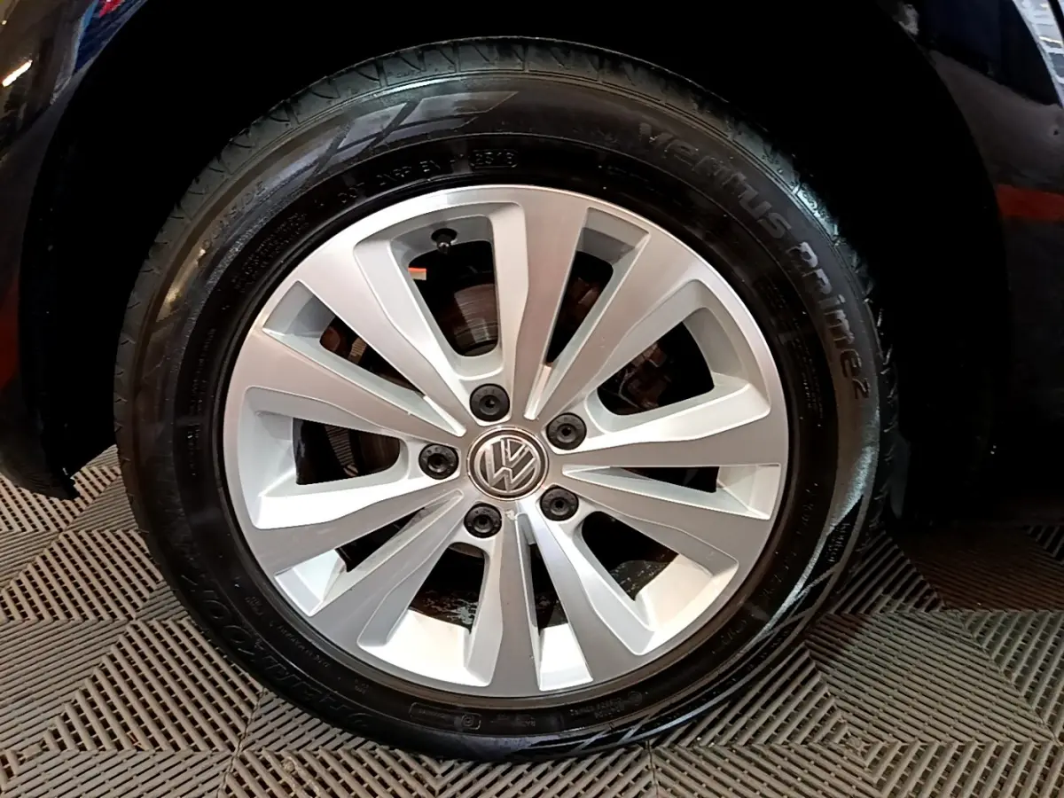 Gros plan sur la roue avant gauche d'une Volkswagen Golf noire, jante alliage argentée à 10 branches.