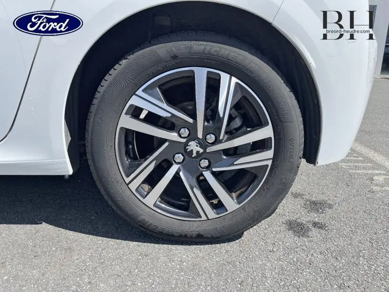 Gros plan sur la roue avant gauche d'une Peugeot 208 blanc banquise avec jante alliage noire et argentée.