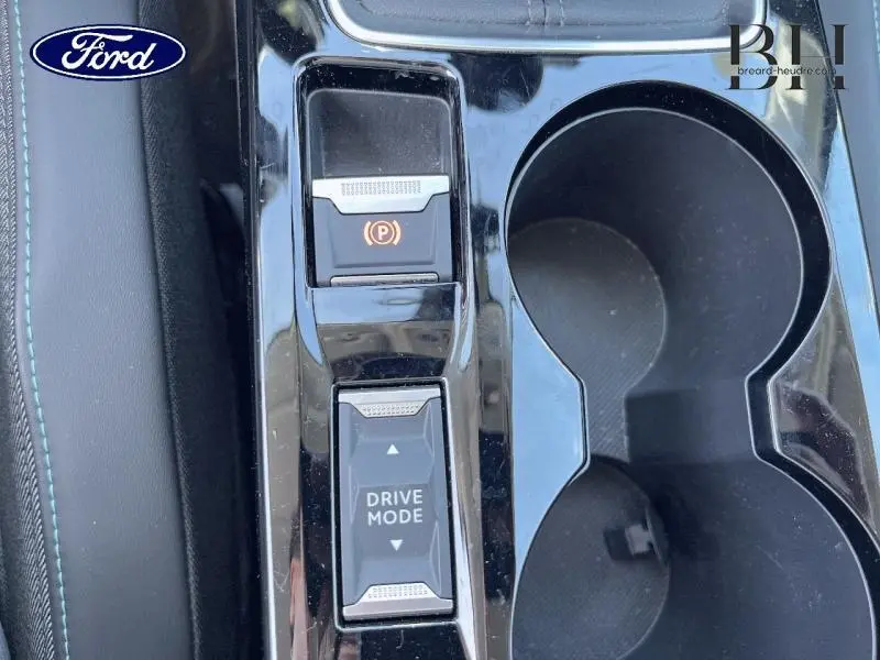 Gros plan sur la console centrale noire avec bouton frein électrique et sélection du mode de conduite.