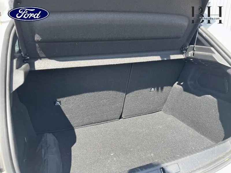 Coffre ouvert vu de l'arrière d'une Peugeot 208 blanc banquise, intérieur noir et tapis de coffre.