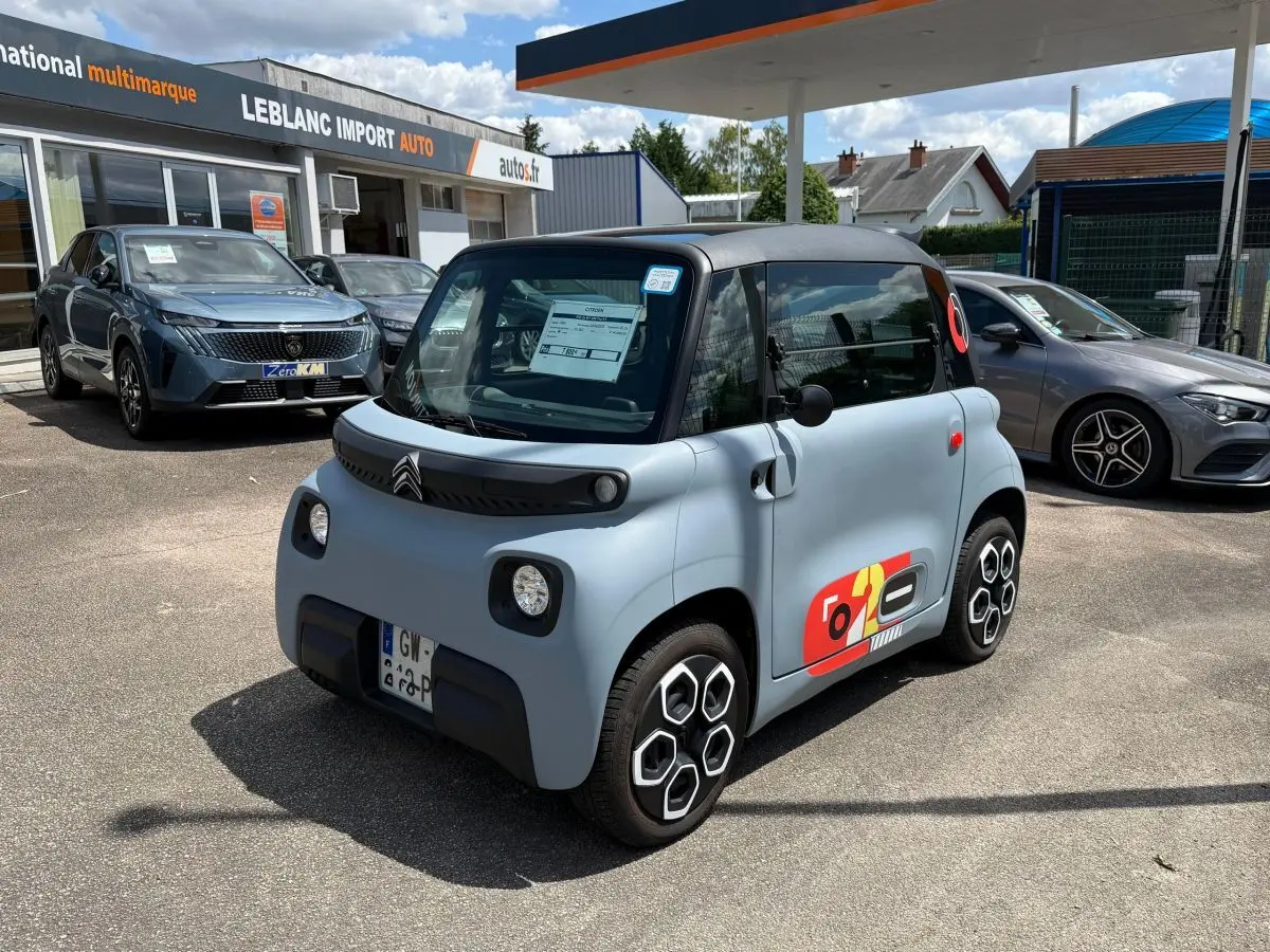 Vue 3/4 avant droite d'une Citroën Ami MY AMI POP électrique gris clair avec toit noir et stickers colorés sur porte.