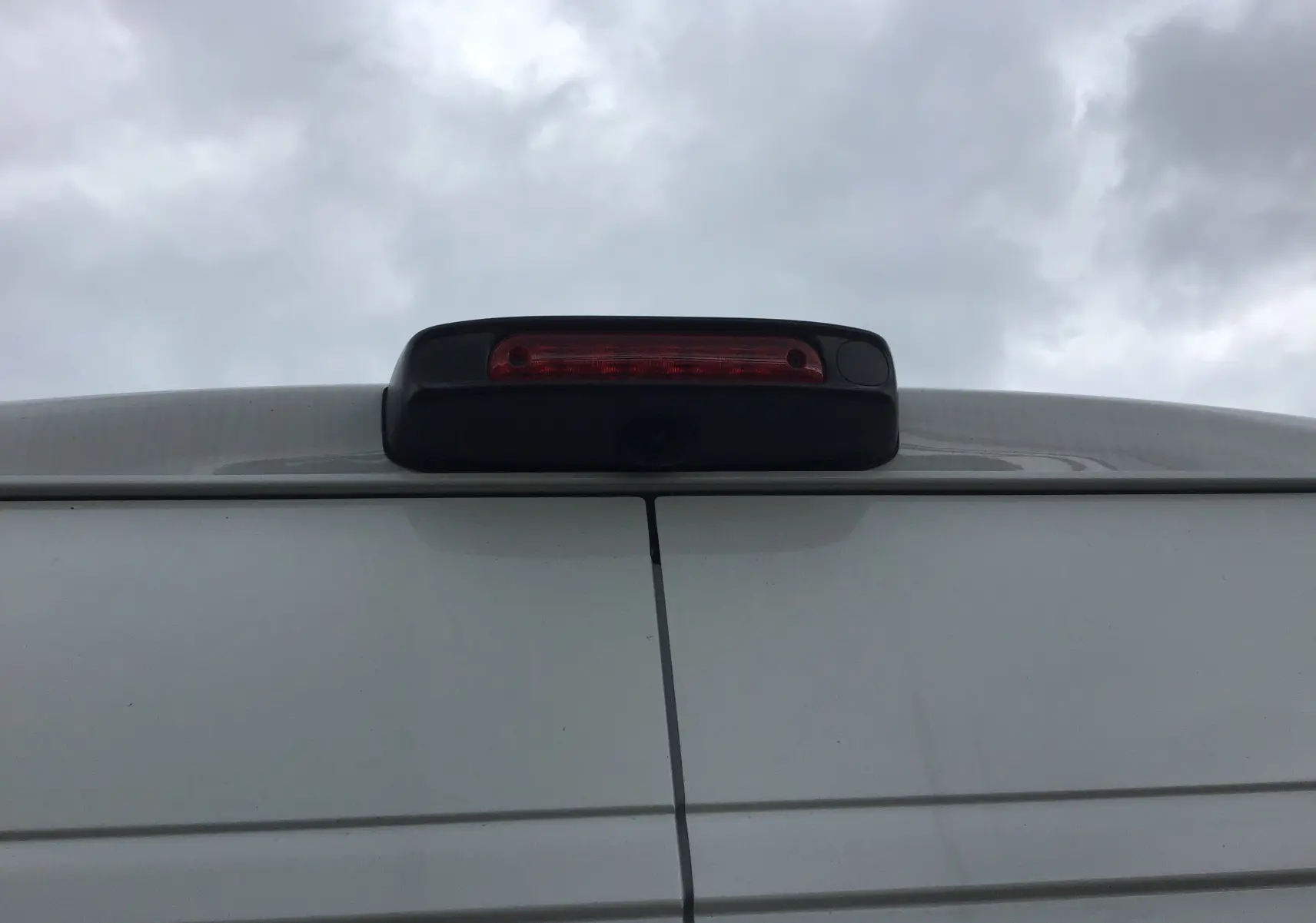 Gros plan sur l'arrière blanc du Peugeot Boxer Fourgon avec feu stop et caméra de recul intégrée sous un ciel nuageux.