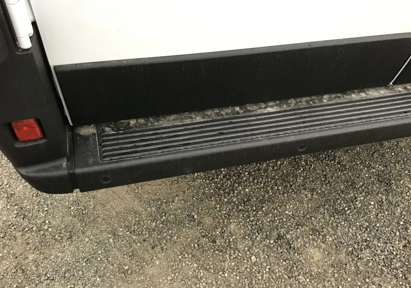 Gros plan sur la marche latérale noire du côté gauche d’un Peugeot Boxer Fourgon blanc, avec traces de boue.