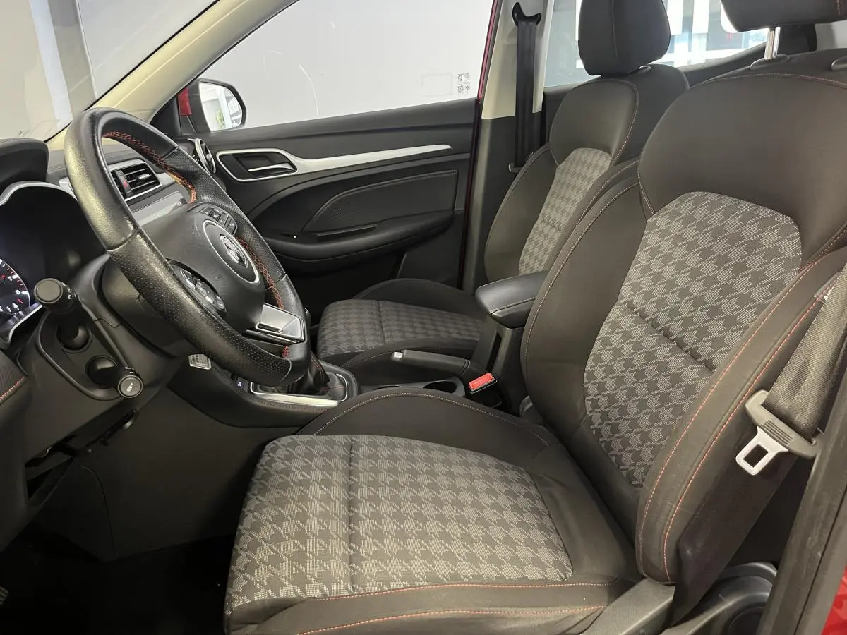 Intérieur côté conducteur du MG ZS rouge 2022 montrant sièges tissu à motif pied-de-poule et volant cuir avec surpiqûres rouges.