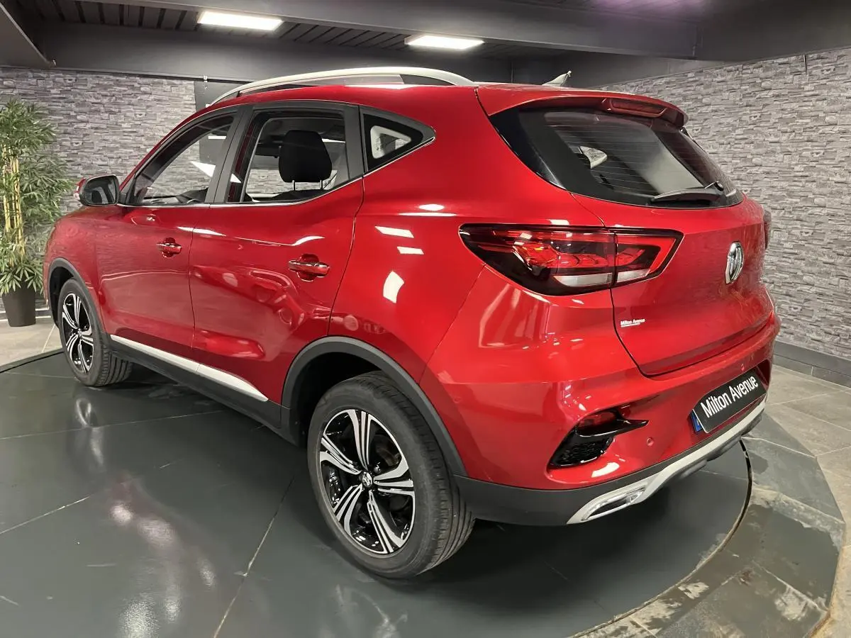 Vue 3/4 arrière droite du SUV MG ZS rouge métallisé avec jantes alliage noires et feux arrière LED dans un showroom.