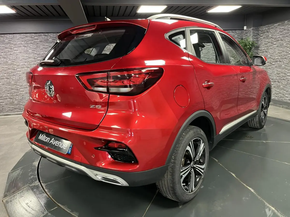 Vue 3/4 arrière droite du MG ZS rouge métallisé avec jantes alliage noires et feux arrière LED dans un showroom.