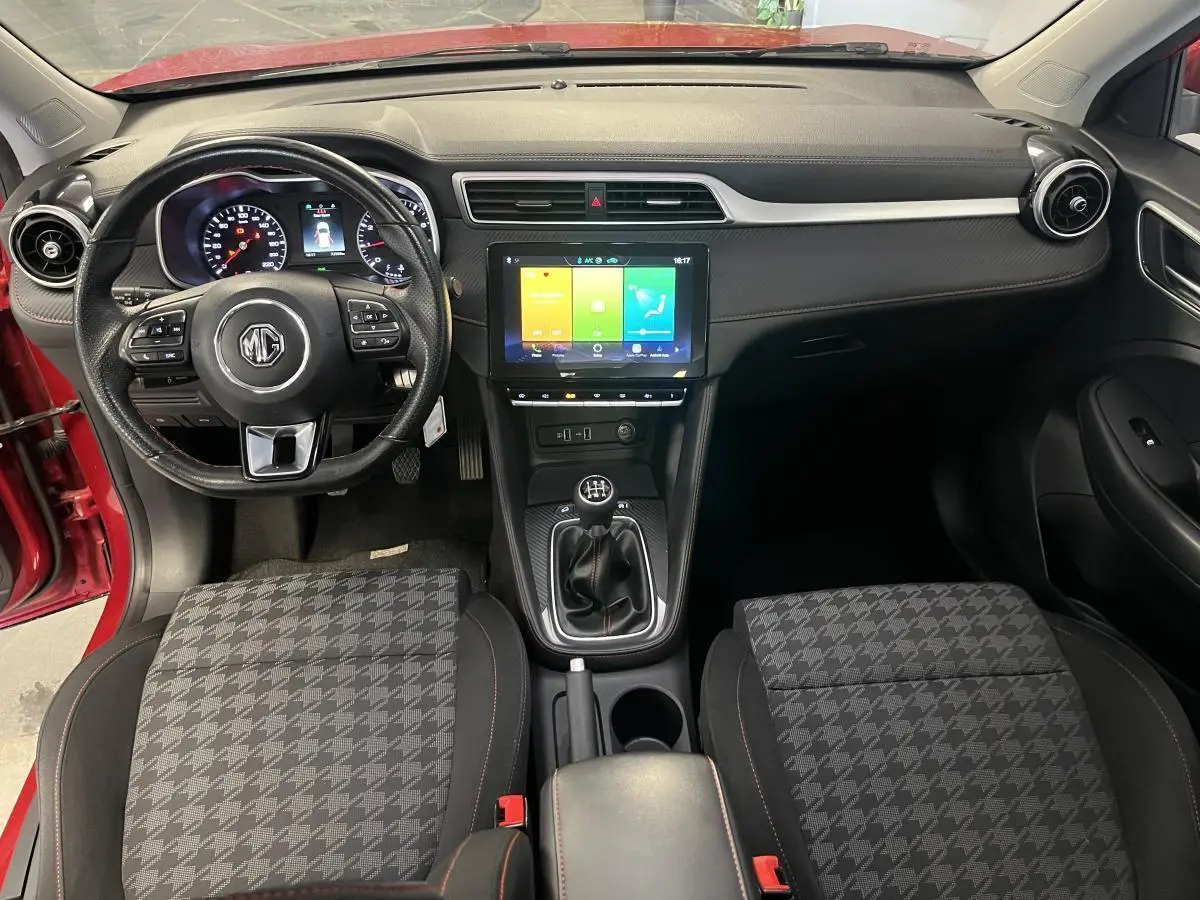 Vue intérieure avant du MG ZS rouge 2022, avec volant cuir multifonctions, écran tactile central et levier de vitesses manuel.