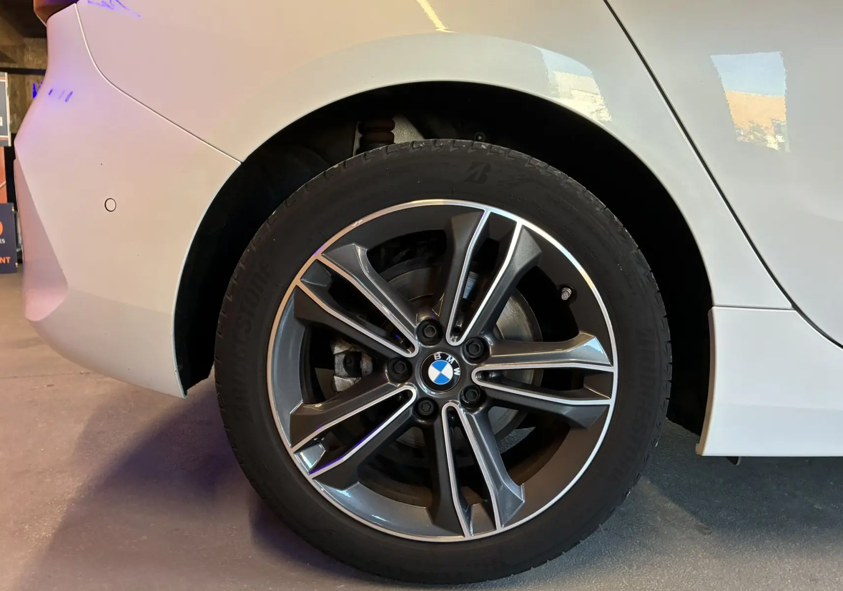 Gros plan sur la roue arrière droite d'une BMW Série 1 blanche, mettant en valeur la jante alliage bi-ton et le logo BMW central.