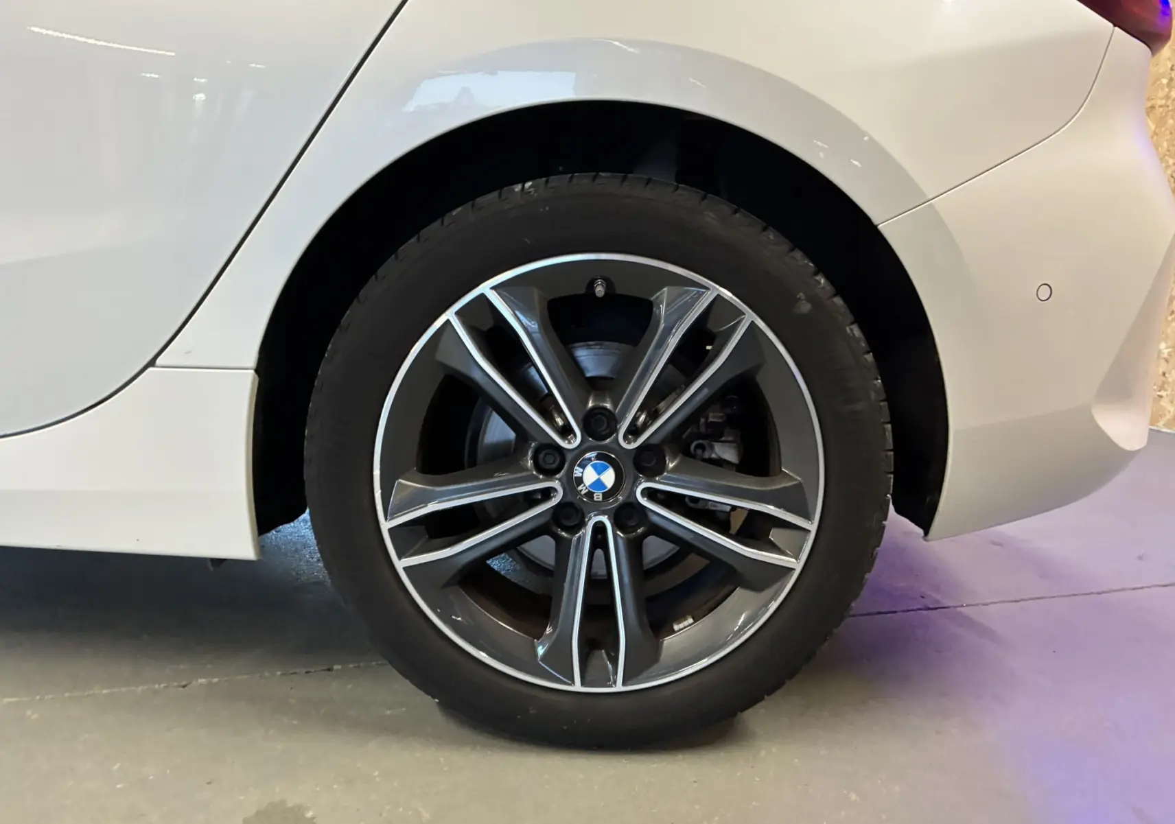 Gros plan sur la roue arrière droite blanche d'une BMW Série 1 118i Edition Sport avec jante alliage bicolore.