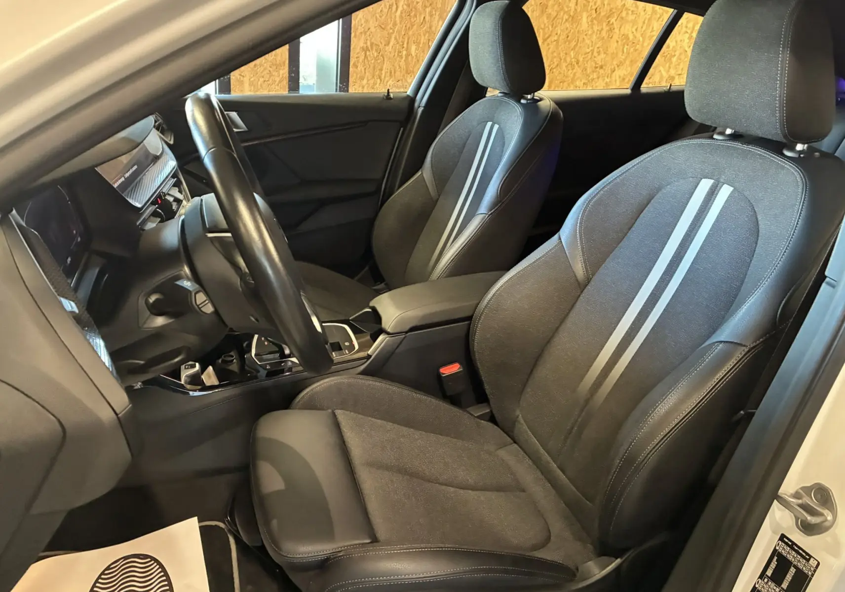 Intérieur noir de la BMW Série 1 118i Edition Sport 2023, vue côté conducteur avec sièges tissu et cuir à bandes grises.